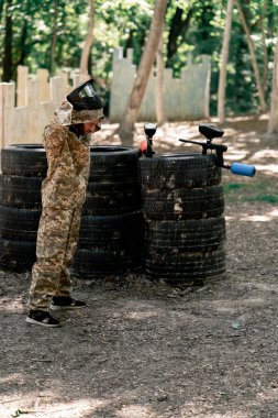 Vasiyetnamede pintball forması giyen bir oyuncu kırmızı balon takım kıyafeti giymiş bir tabanca tutuyor.