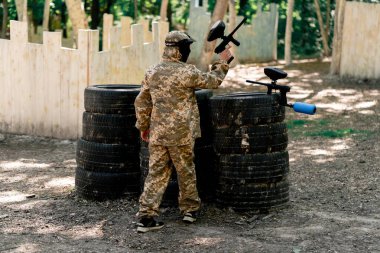 Vasiyetnamede pintball forması giyen bir oyuncu kırmızı balon takım kıyafeti giymiş bir tabanca tutuyor.
