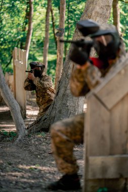 Vahşi doğada ağaçların yanında pintball forması giyen bir oyuncu balon takımı kamuflaj kıyafet iletişimi için ellerini kullanarak tabanca tutar.