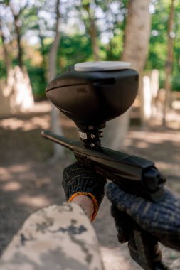 Vahşi doğada ağaçların yanında çömelmiş pintball üniformalı bir oyuncu balonla tabanca tutuyor profesyonel hava tabancasını hedef alıyor