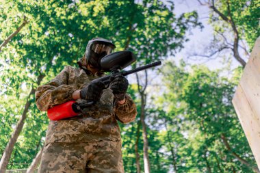 Ağaçların yakınındaki vahşi doğada tilt üniformalı bir oyuncu kırmızı balon takım kıyafetleriyle bir tabanca tutuyor.