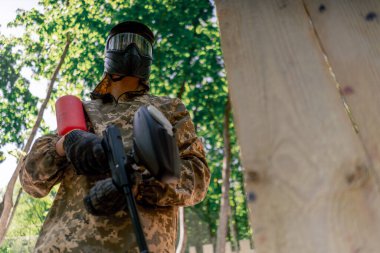 Ağaçların yakınındaki vahşi doğada tilt üniformalı bir oyuncu kırmızı balon takım kıyafetleriyle bir tabanca tutuyor.