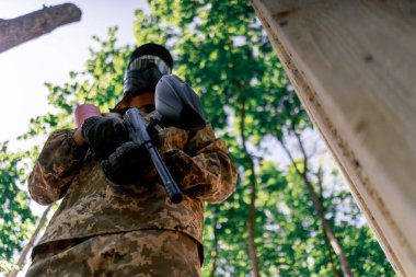 Ağaçların yakınındaki vahşi doğada tilt üniformalı bir oyuncu kırmızı balon takım kıyafetleriyle bir tabanca tutuyor.