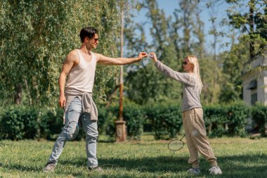 Dışarıda ağaçlarla dolu bir parkta sarışın bir kızla genç bir esmer adam bambinton oynuyorlar en iyi arkadaşlar birlikte rahatlayıp mekiklerin önünden geçiyorlar.