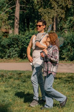 Parkta ağaçlarla kaplı bir parkta esmer bir adam kıvırcık esmer bir kızın yanında duruyor. Bambinton raketleri en iyi arkadaşlar birlikte dinleniyor.