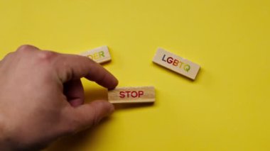 Gölgeleri olmayan sarı, sıcak bir arka plan. Erkek eli, renkli kelimelerle ahşap küpler döşedi. Cinsiyeti durdurun LGBTQ sözcüğünü ortaya koydu.
