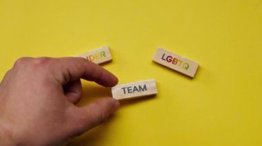 Gölgeleri olmayan sarı, sıcak bir arka plan. Erkek eli, siyah kelimeli ahşap küplerle LGBTQ cinsiyetini ortaya koydu.