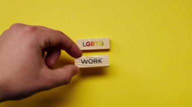 Gölgeleri olmayan sarı, sıcak bir arka plan. Erkek eli, LGBT 'nin çalışmalarını ortaya koyan renkli kelimelerle dolu tahta küpleri yerleştirdi.