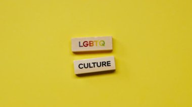 Gölgeleri olmayan sarı, sıcak bir arka plan. Erkek eli, LGBT kültürünü ortaya koyan renkli kelimelerle ahşap küpleri yerleştirdi.