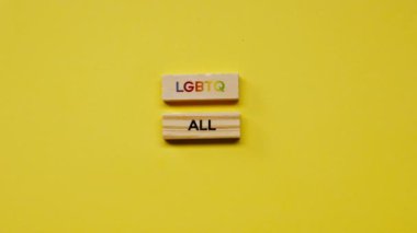 Gölgeleri olmayan sarı, sıcak bir arka plan. Erkek eli, LGBT 'nin tüm cinselliğini ortaya koyan renkli kelimelerle bezenmiş ahşap küpleri seriyordu.