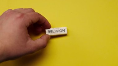 Gölgeleri olmayan sarı, sıcak bir arka plan. Erkek eli, üzerinde renkli kelimeler olan ahşap küpleri ortaya koydu.