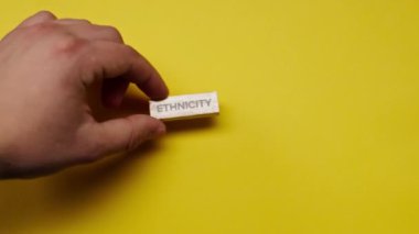 Gölgeleri olmayan sarı, sıcak bir arka plan. Erkek eli, etnik kökenini ortaya koyan renkli kelimelerle ahşap küpleri yerleştirdi.