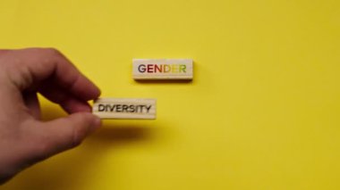 Gölgeleri olmayan sarı, sıcak bir arka plan. Erkek eli, rengarenk kelimelerle bezenmiş tahta küpleri, çeşitlilik cinsiyetini ortaya koydu.