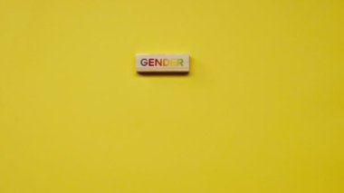 Gölgeleri olmayan sarı, sıcak bir arka plan. Erkek eli, rengarenk kelimelerle bezenmiş tahta küpleri, çeşitlilik cinsiyetini ortaya koydu.