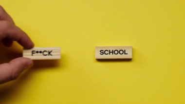 Yellow warm background without shadows the male hand laid wooden cubes with colored words laid out the fuck school