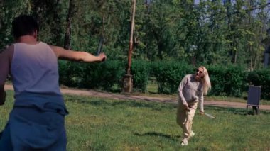 Dışarıda ağaçlarla dolu bir parkta sarışın bir kızla genç esmer bir adam bambinton oynuyor en iyi arkadaşlar birlikte rahatlıyor kız servis yapıyor.