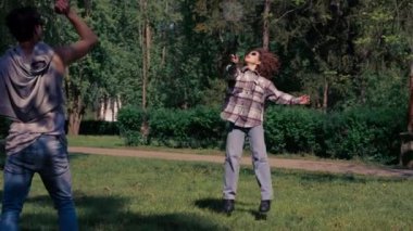 Dışarıda bir parkta ağaçların arasında teslim olma zeminine karşı esmer bir kız raket hareketleriyle servis atıyor.