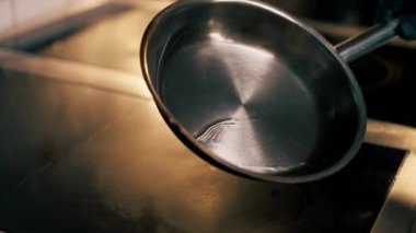 Profesyonel bir mutfakta sıcak fırının üzerindeki küçük bir tavaya yağ döker.