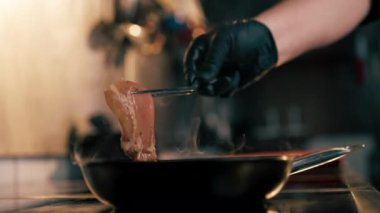 Profesyonel bir sobanın üzerine yakın plan küçük bir tavada şef tavuğu cımbızla filetoya çevirir.