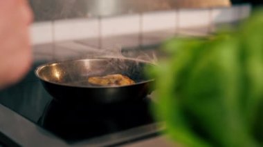 Profesyonel bir mutfakta bir parça tavuk fileto küçük bir tavada kızarır.