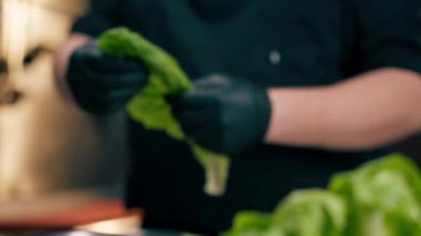 Profesyonel bir mutfakta yakın plan çekimde şef marul yapraklarını demir bir klozete parçalar.