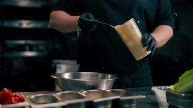 Profesyonel bir mutfakta şef, marul yapraklarının üzerine demir bir kâse döker.