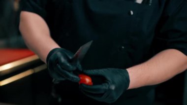 Profesyonel mutfağa yakın çekim yapan şef, küçük bir bıçakla bir domates doğruyor.