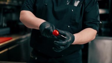 Profesyonel mutfağa yakın çekim yapan şef, küçük bir bıçakla bir domates doğruyor.