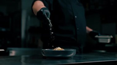 Profesyonel bir mutfakta yakın plan çekimde şef salata tabağı desenli bir kaseye peynir döker.