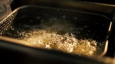 Profesyonel bir mutfakta yakın plan çekimde tavuk kanatlarını fritözde kızartıyorum.