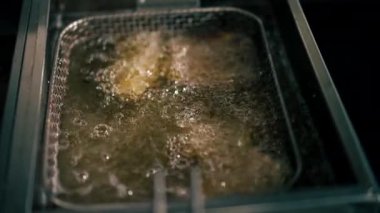 Profesyonel bir mutfakta yakın plan çekimde tavuk kanatlarını fritözde kızartıyorum.
