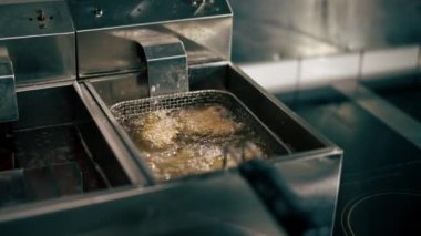 Profesyonel bir mutfakta yakın plan çekimde tavuk kanatlarını fritözde kızartıyorum.