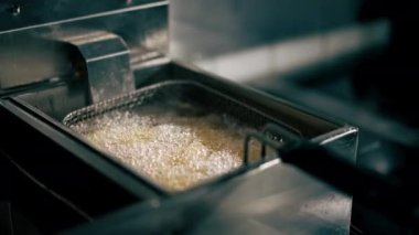 Profesyonel bir mutfakta, yağda patates kızartması pişirirken fritözde şefin sallaması.