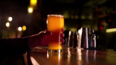 Ahşap bir bar masasına yakın plan bir adam bir bardak light bira tutuyor.