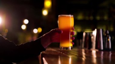 Ahşap bir bar masasına yakın plan bir adam bir bardak light bira tutuyor.