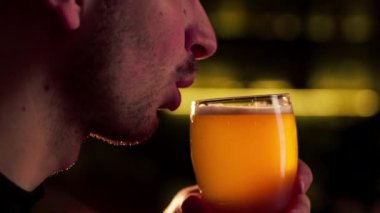 Tahta bar masasına yakın çekim yapan bir adam bir bardak light biradan ılık ışıklandırma ışığı içer.