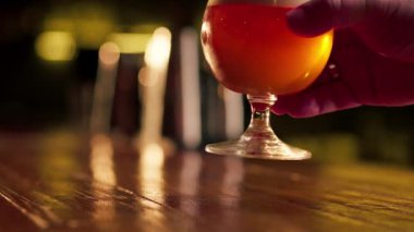 Ahşap bir bar masasına yakın plan bir adam bir bardak light bira tutuyor.