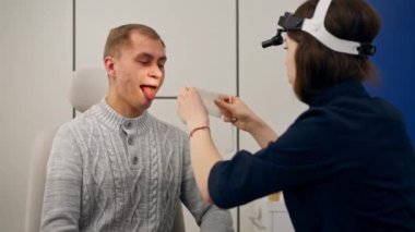 Klinikte genç bir doktor kulağının burun kısmı hastanın boğazını muayene ediyor.