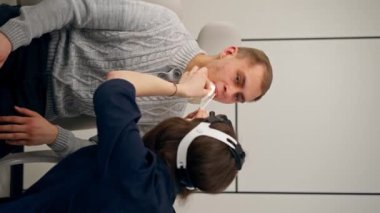 Klinikte genç bir doktorun dikey videosu. Kulak tıkayıcı. Hastanın boğazını muayene ediyor.