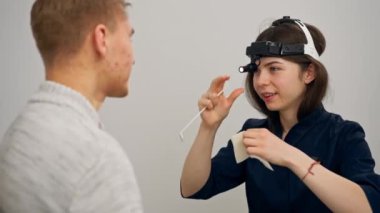 Klinikte genç bir doktor kulağının burun kısmı hastanın boğazını muayene ediyor.
