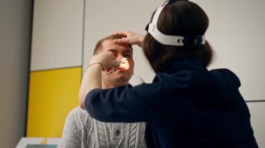 Klinikte genç bir doktor kulağı boğazı, hastanın burnunu ışıklarla muayene eder.