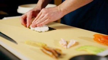 Japon lokantasında mavi üniformalı bir şef sarı bir tahtanın üzerinde balık sarması çeviriyor.