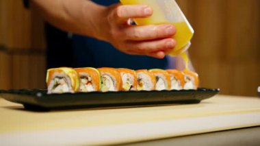 Japon lokantasına yakın plan mavi üniformalı bir şef hazır suşinin üzerine sos döker.