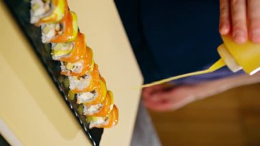 Japon restoranındaki dikey görüntülerde mavi üniformalı bir şef hazır suşinin üzerine sos döker.
