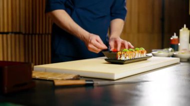 Mavi üniformalı bir Japon restoran şefi hazır suşiyi tabakta süslüyor.