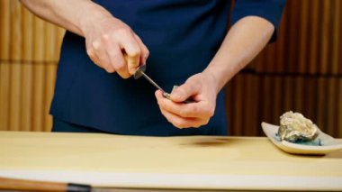Japon restoranında mavi üniformalı bir şef bir istiridyeyi bıçakla açar.