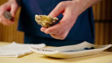 Japon restoranında mavi üniformalı bir şef bir istiridyeyi bıçakla açar.
