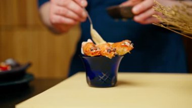 Japon restoranında mavi üniformalı bir şef karidesin üzerine sos döker.