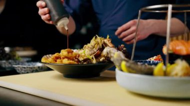 Japon restoranına yakın plan mavi üniformalı bir şef bir tabak deniz ürününe sos döker.