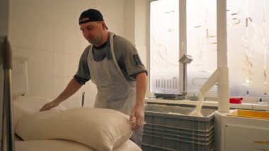 Profesyonel bir mutfakta kapsayıcı bir işçi bir torba unu alır ve yanında taşır.